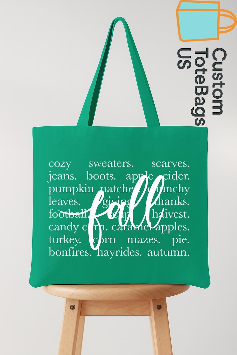 May include: A green tote bag with white text that reads "fall" in cursive. The bag lists fall-themed words like "cozy," "sweaters," "pumpkin patch," and "hayrides." The bag also has the text "Custom Tote Bags US".