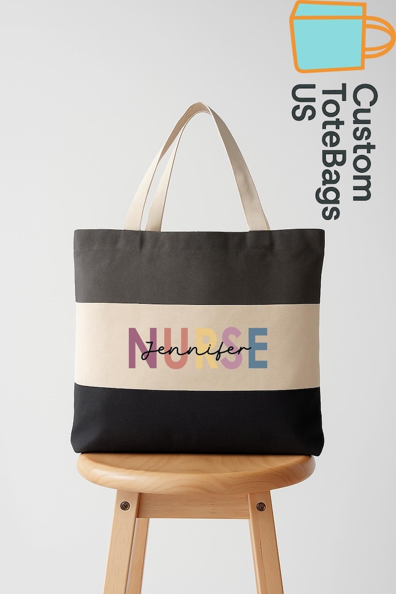 May include: A black, grey, and beige tote bag with the text "NURSE Jennifer" in colorful letters. The bag has beige handles and is sitting on a wooden stool. The words "Custom Tote Bags US" are in the upper right corner.