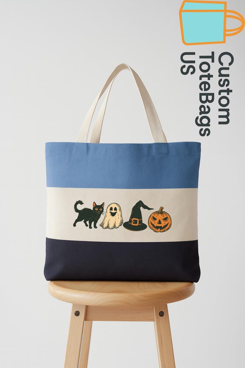 May include: A canvas tote bag with a blue, off-white, and navy color block design. The bag features Halloween-themed illustrations of a black cat, ghost, witch hat, and jack-o'-lantern. The bag has off-white handles and the text "Custom Tote Bags US".