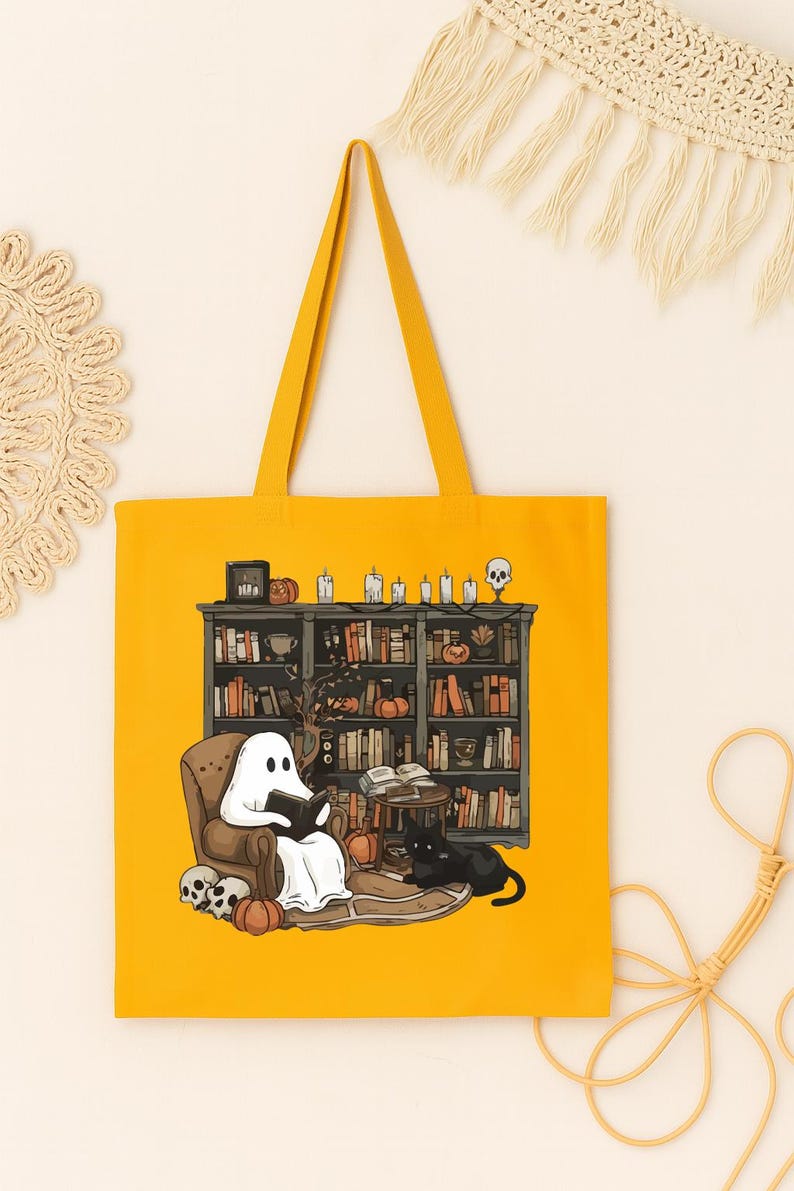 Puede incluir: Bolso tote amarillo mostaza con una ilustraci&oacute;n de un fantasma leyendo en una biblioteca. El dise&ntilde;o incluye un gato negro, calabazas y una estanter&iacute;a con libros, velas y una calavera. El bolso tiene una forma rectangular simple.