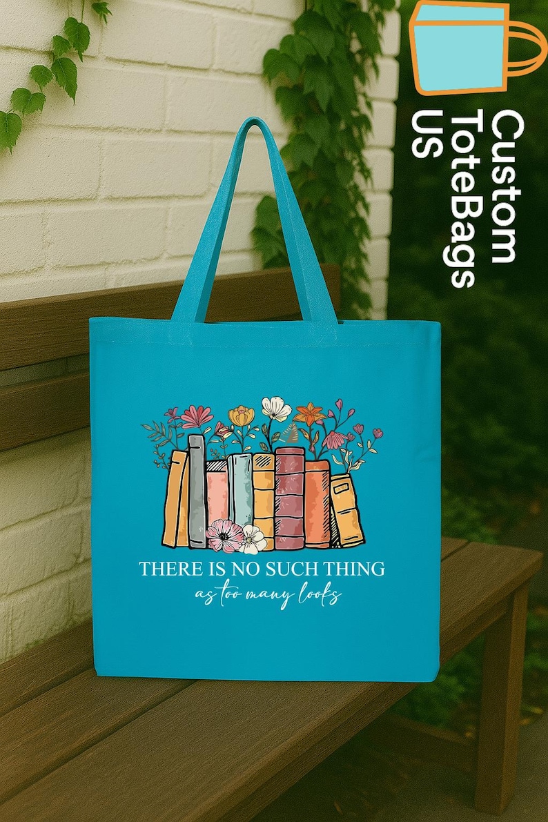 May include: A turquoise tote bag with a design of books and flowers. The text "THERE IS NO SUCH THING as too many books" is printed on the bag. The bag has turquoise handles and is on a wooden bench.