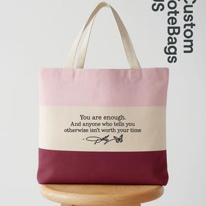 May include: A color-blocked tote bag featuring three horizontal stripes in light pink, cream, and deep burgundy. The center cream stripe displays the black text: You are enough. And anyone who tells you otherwise isn't worth your time - Polly.