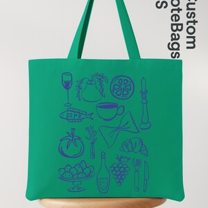 May include: A green tote bag with blue illustrations of food items like a wine glass, fish, and grapes. The bag has long handles and the text "Custom Tote Bags US" in a vertical orientation.