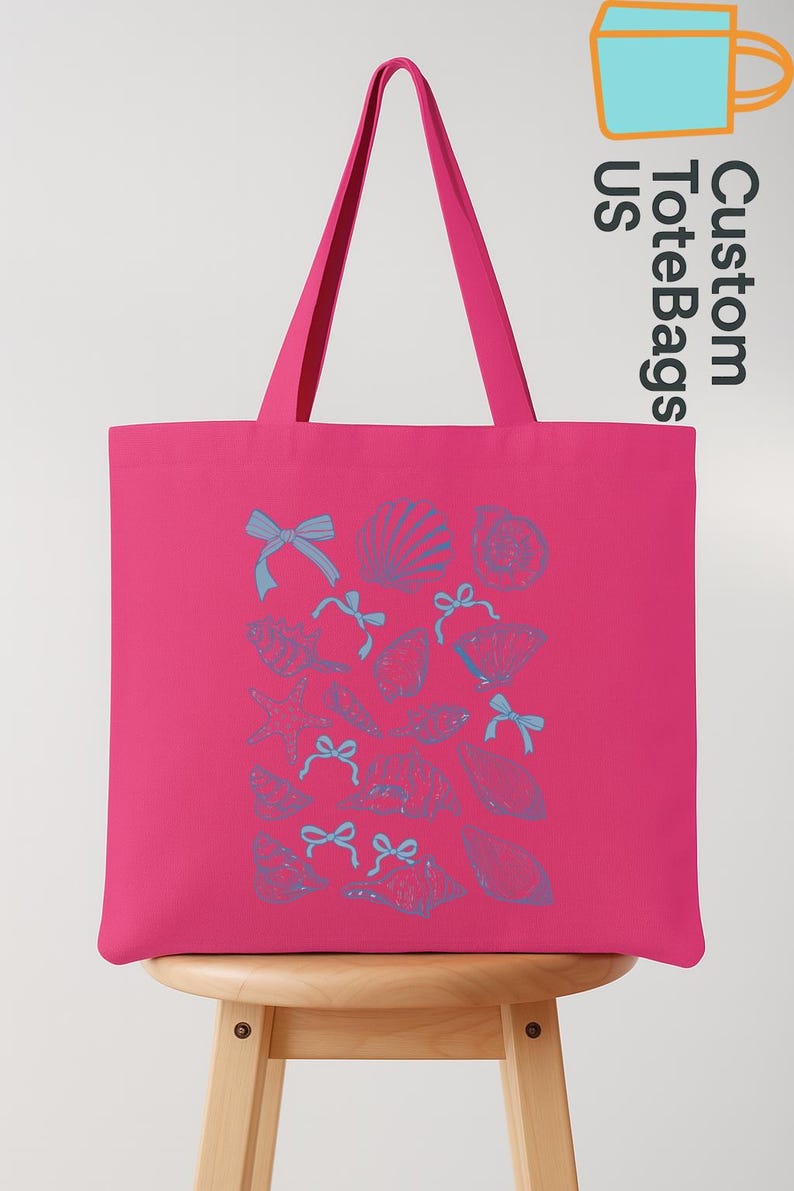 K&ouml;nnte beinhalten: Eine leuchtend pinkfarbene Tragetasche mit blauen Muschel- und Schleifenillustrationen. Die Tasche hat lange Henkel und der Text "Custom Tote Bags US" ist auf der Seite aufgedruckt. Die Tasche steht auf einem Holzschemel.