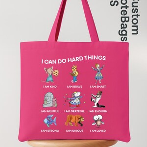 May include: A pink tote bag with the text "I CAN DO HARD THINGS" and illustrations of cartoon characters with positive affirmations. The bag also has the text "Custom ToteBags US".