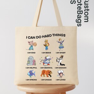 May include: Beige tote bag with the text "I CAN DO HARD THINGS" and illustrations of cartoon animals with positive affirmations like "I AM KIND" and "I AM BRAVE". The bag also has the text "Custom ToteBags US".