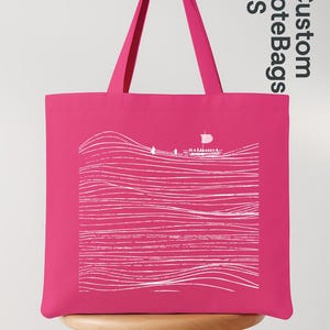 Puede incluir: Un bolso tote rosa brillante con un dibujo lineal blanco que representa un paisaje marino con un velero. El bolso tiene asas rosas a juego y el texto "Custom ToteBags US".