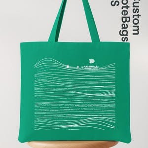 Puede incluir: Un bolso tote verde con un gr&aacute;fico blanco de un barco navegando sobre l&iacute;neas onduladas. El bolso tiene un asa verde a juego y el texto "Custom ToteBags US" est&aacute; impreso en el lateral.