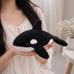 Könnte beinhalten: Ein handgefertigtes gehäkeltes Orca-Plüschtier mit schwarzem Oberkörper, weißem Bauch, einer Rückenflosse und zwei Seitenflossen. Der Orca hat einen kleinen weißen Fleck in der Nähe des Auges und ein dunkles, rundes Auge aus strukturiertem Garn.