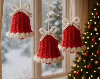 May include: Three handmade, red crocheted bell ornaments with white bows and trim hang in front of a window. A Christmas tree with red and gold ornaments is visible in the background. The bells are suspended by white cords.