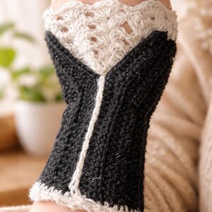 Könnte beinhalten: Gehäkelte Handgelenkwärmer in Schwarz und Off-White. Die Handgelenkwärmer haben einen schwarzen Körper mit einem weißen vertikalen Streifen und eine gewellte, cremefarbene Manschette. Der obere Teil ist ein Spitzendesign.