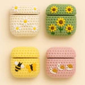 Könnte beinhalten: Vier gehäkelte AirPod-Hüllen. Die Hüllen sind cremefarben mit Gänseblümchen, grün mit Sonnenblumen, gelb mit Bienen und Schmetterlingen und rosa mit Schnecken. Jede Hülle hat einen passenden Deckel.