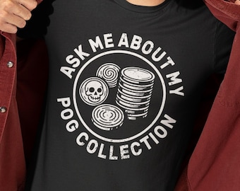 May include: A black t-shirt featuring a white circular graphic with the text "ASK ME ABOUT MY POG COLLECTION" surrounding illustrations of a skull-themed pog, a single pog, and a tall stack of pogs, worn under a dark red button-down shirt.