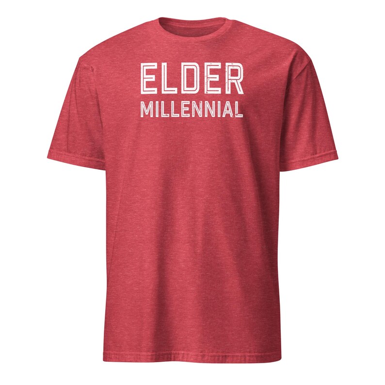 May include: A heathered red short-sleeve t-shirt featuring the text ELDER MILLENNIAL printed in white block letters across the chest. The shirt has a crew neckline and a standard fit, showcasing a textured fabric appearance throughout the garment.