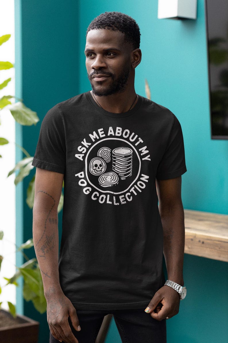 Puede incluir: Camiseta negra con un dise&ntilde;o gr&aacute;fico blanco que dice "ASK ME ABOUT MY POG COLLECTION". El dise&ntilde;o incluye una calavera y pogs apilados. La camiseta es de manga corta.