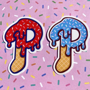 May include: Two stickers shaped like the letter "P" with a dessert theme. One is red with white sprinkles and the other is blue with blue sprinkles. The bottom of each letter is a waffle cone shape.