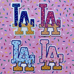 May include: Four LA stickers in blue, red, light blue, and pink, with a dripping icing design and sprinkles. The letters sit on a waffle cone base, all on a pink background with colorful sprinkles.