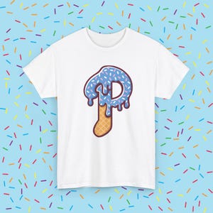May include: White t-shirt featuring a blue letter "P" designed as a dripping donut with sprinkles, atop a waffle cone. The shirt is set against a light blue background with colorful sprinkles.