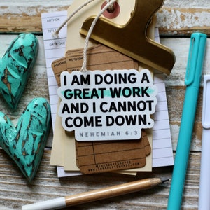 May include: A white sticker with teal accents reads "I am doing a great work and I cannot come down. Nehemiah 6:3". The sticker is on a stack of paper with a gold binder clip.