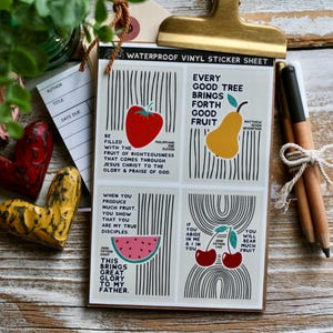 Pode incluir: Uma folha de adesivos de vinil à prova d'água com ilustrações de frutas e texto inspirador. A folha apresenta um morango vermelho, uma pera amarela, uma fatia de melancia e cerejas. O texto inclui versículos bíblicos.