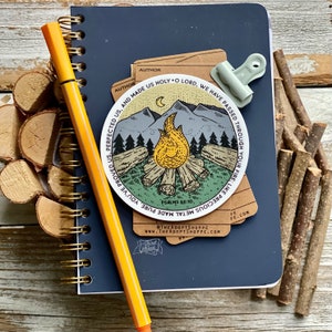 May include: A round sticker with a campfire scene, mountains, and a crescent moon. The sticker has the text "You're made pure metal, you're perfected us, and made us holy, O Lord, we have passed through your fire, like precious metal." and "Psalms 66:10".