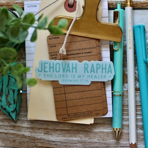 May include: A blue and white sticker with the text "Jehovah Rapha + The Lord is my Healer + Jeremiah 17:14" on a brown card with the text "@THEADOPTSHOPPE WWW.THEADOPTSHOPPE.COM".
