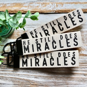 May include: Three white canvas keychains with black text that reads "He Still Does Miracles".