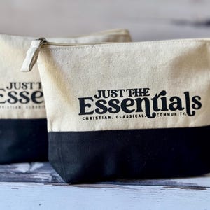 May include: Two beige canvas zippered pouches with black bottoms. The pouch on the right has the text "Just the Essentials" in black lettering with the words "Christian, Classical, Community" underneath.