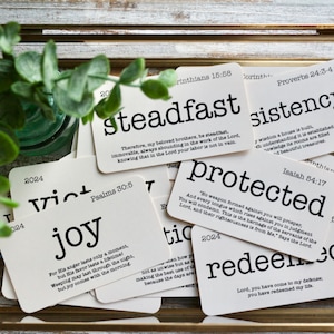 May include: A collection of white cards with black text, each featuring a different word and bible verse. The words include "steadfast", "consistency", "victory", "joy", "protected", and "redeemed".