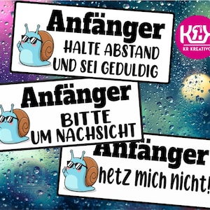 Op de afbeelding: Drie witte rechthoekige borden met zwarte tekst en cartoon slak illustraties. De borden luiden "Anfänger" met verschillende zinnen: "HALTE ABSTAND UND SEI GEDULDIG", "BITTE UM NACHSICHT" en "hetz mich nicht!". Een roze logo staat rechtsboven.