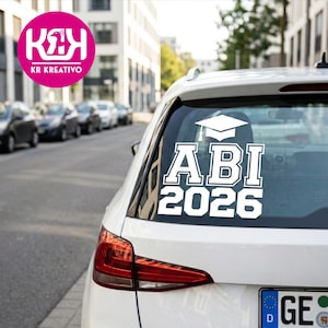 Könnte beinhalten: Weißer Autoaufkleber mit dem Text "ABI 2026" in fetter Schrift, gekrönt von einer Abschlusskappe. Der Aufkleber befindet sich auf der Heckscheibe eines weißen Autos, mit einer Straße im Hintergrund.