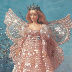May include: A doll wearing a pink sequined gown with matching wings and a jeweled crown. The doll has blonde hair and is adorned with sequins and beads. The dress has long sleeves and a full skirt, creating a fairy-like appearance.