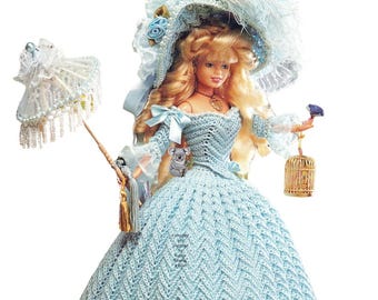 May include: A doll in a pale blue crocheted gown, matching hat, and parasol. The doll has blonde hair and is holding a small bird and a gold birdcage. A small koala bear is attached to the dress. The dress has a chevron pattern.