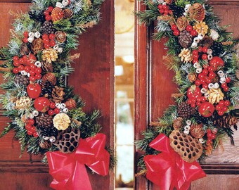 May include: Two crescent-shaped holiday wreaths featuring green pine needles, red berries, brown pinecones, and dried lotus pods. Each wreath is accented with a large, bright red ribbon bow with long, flowing tails, mounted on a dark wood door.