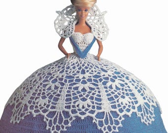 May include: A Barbie doll in a handmade crochet dress. The dress has a white bodice with blue trim, a white lace collar, and a full skirt in blue and white. The doll has blonde hair styled in an updo.