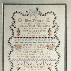 May include: Cross-stitch sampler featuring the Lord's Prayer, framed with a decorative border. The text is in black thread on a cream-colored background, with floral and religious motifs.