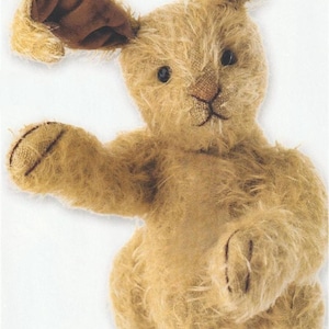 May include: A plush, tan-colored bunny rabbit toy with long, brown-lined ears and a stitched nose. The bunny has a soft, textured appearance and is posed with one arm extended.
