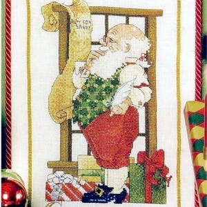 Puede incluir: Tapiz navideño de punto de cruz que representa a Papá Noel con una lista, regalos y la inscripción "Christmas List". Papá Noel lleva un chaleco verde, pantalones rojos y botas negras. El diseño incluye una guirnalda verde y una cinta roja.