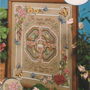 May include: A framed cross-stitch sampler with floral and butterfly designs. The sampler includes the text "The desert shall rejoice" and "And blossom as the rose." The design features pink, yellow, and red roses, and blue and yellow butterflies.