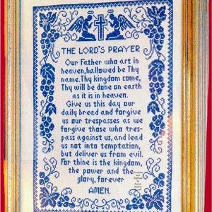 May include: A framed cross-stitch sampler featuring The Lord's Prayer in blue thread on white fabric. The design includes two angels, a cross, and grape vine borders. The text reads: THE LORD'S PRAYER, Our Father who art in heaven, hallowed be Thy name.