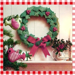 May include: A fabric wreath made of green patterned leaves and small red berries, featuring a large red bow. Two plush bird ornaments hang nearby, one light green with pink wings and one pink with white stripes. Text reads Compiled & Digitised by Aussie Sewing & Crafts.