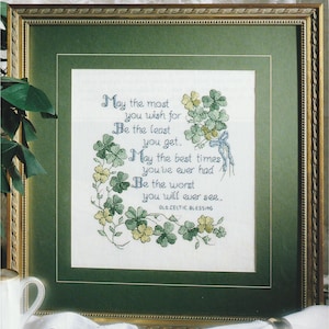 May include: Framed cross-stitch artwork featuring a Celtic blessing. The text, in blue thread, reads "May the most you wish for be the least you get. May the best times you've ever had be the worst you will ever see." Green shamrocks adorn the design.