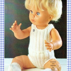 Puede incluir: Una muñeca de cabello rubio y ojos azules que viste un mameluco blanco de punto sin mangas y calcetines blancos a juego. Un pequeño broche de koala está sujeto al pecho. El texto Compiled and Digitised by Aussie Sewing & Craft es visible.