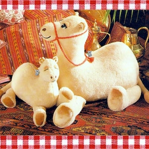 May include: Two cream-colored plush camel toys, one large and one small, featuring soft fur, brown foot pads, and a red rope halter on the larger camel. The text "Designed and Copyrighted by Aussie Sewing & Craft" is visible on the lower right side.