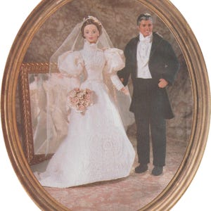 May include: An oval framed image of a bride and groom doll. The bride is in a white wedding dress with a veil and a bouquet. The groom wears a black tuxedo. The frame is gold-coloured.