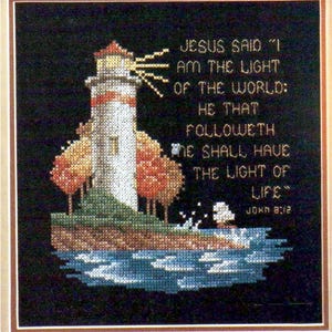 May include: A cross-stitch embroidery on a black background featuring a white lighthouse with a yellow light beam, orange trees, and blue water. The text reads: JESUS SAID "I AM THE LIGHT OF THE WORLD: HE THAT FOLLOWETH ME SHALL HAVE THE LIGHT OF LIFE" JOHN 8:12.