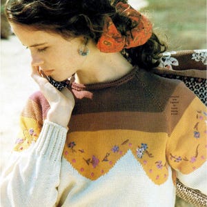 May include: A long-sleeved knit sweater featuring horizontal color-blocked stripes in cream, mustard yellow, and dark brown. The sweater is decorated with embroidered floral motifs and a small koala figure. Text reads: Compiled and Digitized by Aussie Sewing & Craft.
