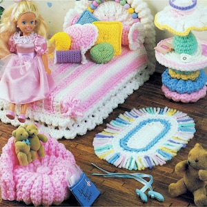May include: A doll and miniature crocheted furniture set. The set includes a pink and white striped bed, a pink chair, a rug, a lamp, and a teddy bear. The doll is wearing a pink dress.