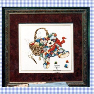 May include: A framed cross-stitch artwork featuring a patchwork teddy bear sitting next to a woven basket filled with sewing spools, scissors, and thread. The text Compiled & Digitised by Aussie Sewing & Crafts is printed on the white fabric.