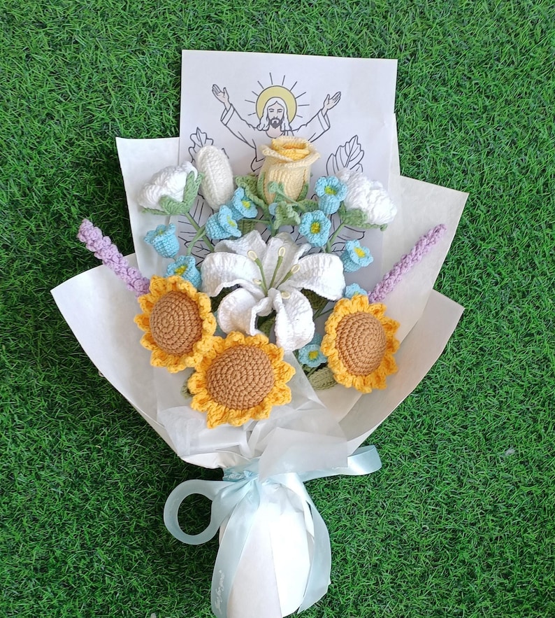 Puede incluir: Un ramo de flores de ganchillo envuelto en papel blanco. El ramo incluye girasoles, lirios, rosas y nomeolvides. Se incluye una peque&ntilde;a tarjeta con un dibujo de Jes&uacute;s.